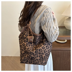 Detail of a large leopard print tote bag with brown leather trim and mini pouch accessory