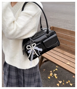 Detail of black glossy shoulder bag with bow charm and lace ribbon on a white sweater