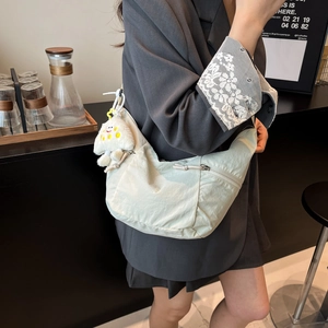 Minimalist nylon dumpling crossbody bag with plush charm on charcoal blazer background