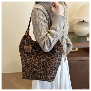 Detailed view of leopard print tote bag with brown leather straps on model's shoulder