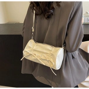 Detail of creamy white pillow bag with shirring and bow decoration on leather surface