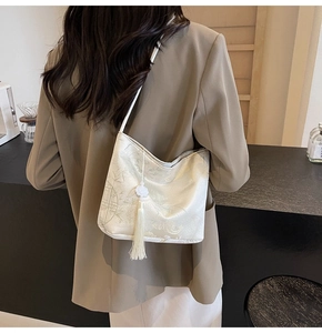 Detail of a chic cream jacquard bucket bag with fringe tassel shown on model's shoulder