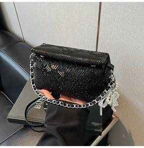 Detail of black snake-embossed square bag with silver chain and pearl lace charm