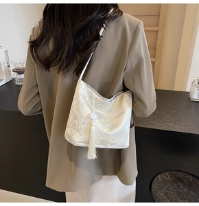 Detail of cream brocade bucket bag with floral patterns and a long white silk tassel