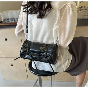 Detail of black leather pillow bag featuring side pleats and decorative ribbon bows