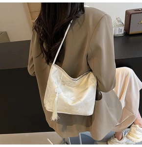 Detail of elegant cream jacquard crossbody bag featuring traditional embroidery and tassel
