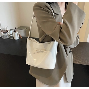 Close-up of a white glossy patent leather shoulder bag with a cute bow detail
