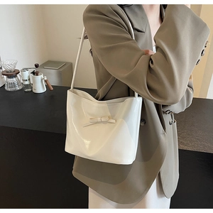 Close-up of a white glossy faux leather shoulder bag with a stylish bow decoration