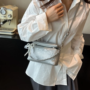 Silver scale textured crossbody bag with chain and pearl bow charm shown on model