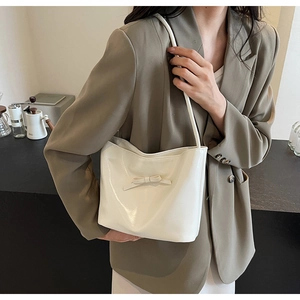 Detail of a creamy white glossy bucket bag with a chic 3D bow on a model in a cafe