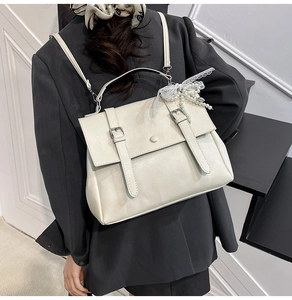 Close-up of cream leather backpack featuring metal buckles and lace pearl pendant detail