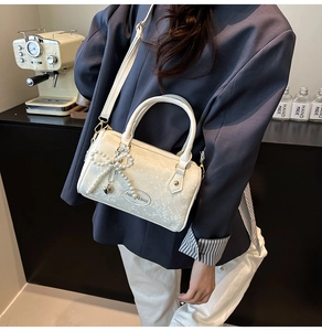Detail of off-white quilted Boston bag with pearl bow charm and heart metal pendant
