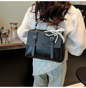 Detail of black flap shoulder bag with white lace bow and pearl bead charms on faux leather