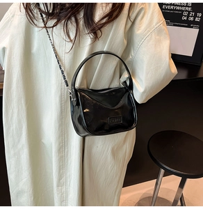 Detail of glossy black leather crossbody bag with silver chain and Fashion label
