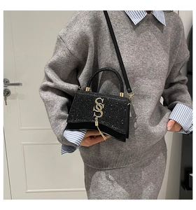 Dettaglio borsa nera con patta glitterata, logo S dorato e ciondolo con nappe lunghe