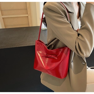 Close-up of red patent leather shoulder bag with bow detail worn under the arm