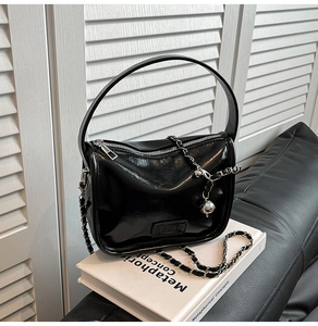 Close-up of black glossy leather crossbody bag with chain strap and embossed Fashion logo