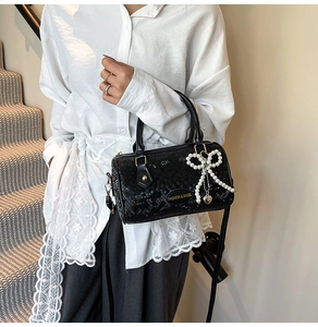 Detail of black snake-textured pillow bag with pearl bow and heart charm on a model