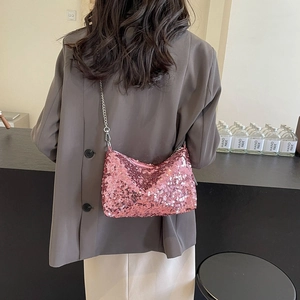 Pink sequined shoulder bag with metallic chain strap worn by a model in a minimalist setting