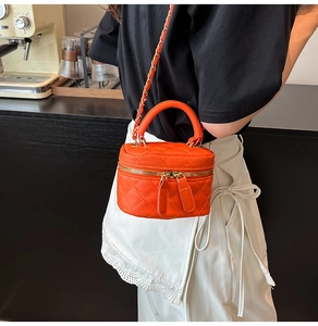 Detail of orange quilted mini crossbody bag with gold-tone chain strap on a model
