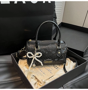 Detail of a black snake-pattern pillow bag with pearl bow charm and gold hardware