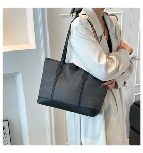 Model wearing a large dark grey tote bag with black leather straps and minimalist design