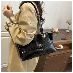 Detail of a shiny black patent leather shoulder bag with silver buckle on khaki trench coat