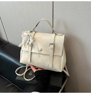 Detail of off-white leather handbag with pearl bow charm and decorative buckles