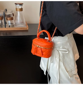 Detail of orange quilted mini vanity bag with gold chain strap on female model