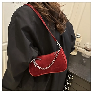 Detail of burgundy suede baguette bag with silver chain and rhinestone bow on a model