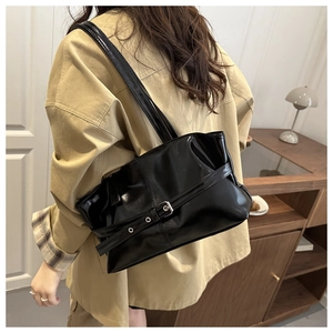 Glossy black shoulder bag with silver metallic buckle detail shown on person