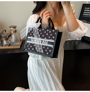 Detail of black tote bag featuring white bow patterns and lace ribbon on leather handle
