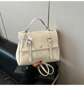 Detail of cream faux leather handbag featuring pearl lace bow charm and strap handle