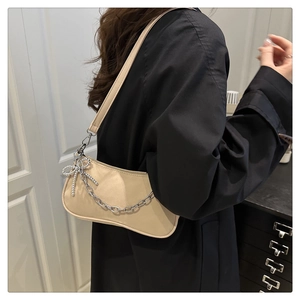 Détail du sac sous le bras beige minimaliste avec chaîne argentée et pendentif nœud