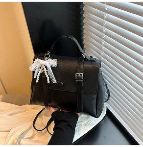 Detail of black leather handbag with decorative lace bow and pearl charm accessory