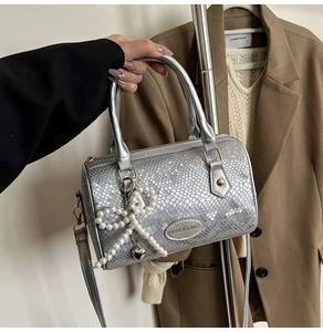 Detail of silver snake-pattern pillow bag featuring pearl bow and heart charms