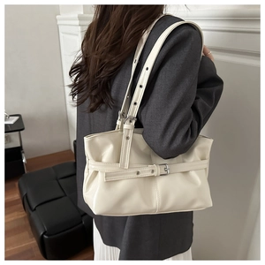 Model wearing a cream PU leather shoulder bag with adjustable eyelet strap and metal buckle