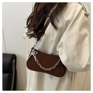 Détail d'un sac bandoulière en daim marron foncé avec chaîne argentée et nœud strass