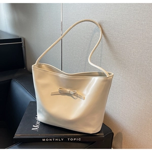 Detail of a creamy white tote bag with a bow accent on a minimalist dark sofa