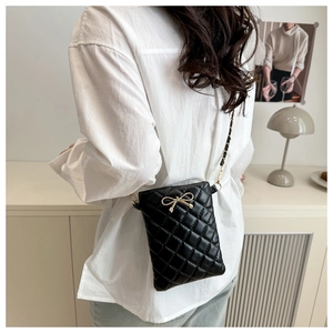 Détail du sac bandoulière matelassé noir avec nœud doré et bandoulière chaîne