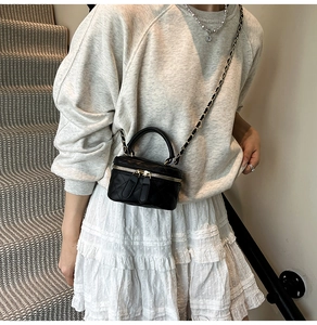 Close-up of black quilted cylinder bag with gold chain strap worn by a model