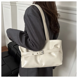Detail of a creamy white patent leather tote bag with decorative strap buckle on a model