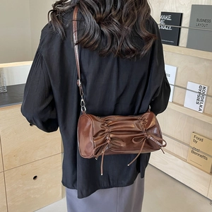 Brown pleated cylinder bag with bow details worn by a model in a minimalist urban setting