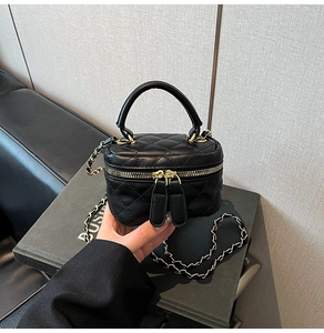 Close-up of black quilted cylindrical bag with gold metal handle and chain strap