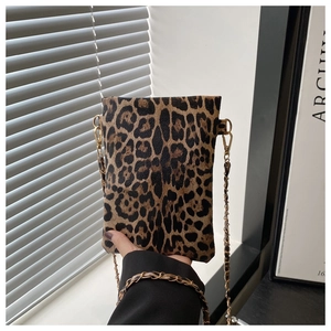 Close-up of leopard print crossbody bag with gold chain strap held against art background