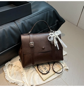 Detailed view of dark brown faux leather bag with lace pearl bow and buckle straps