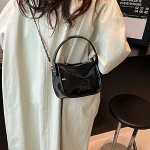 Minimalist black glossy crossbody bag with silver chain and top handle on cream trench coat