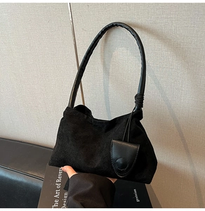 Detail of minimalist black suede shoulder bag with leather handle and decorative mini pouch