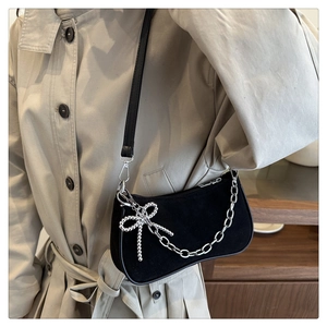 Detail of black suede baguette bag with silver chain and pearl bow charm accessory