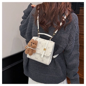 Detail of white monogrammed backpack with a cute plush bear charm on a model's shoulder
